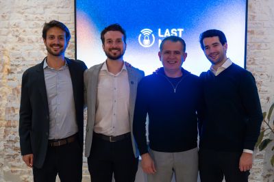 Grupo de quatro pessoas diante de tela “Last” Quatro pessoas posam lado a lado em um ambiente interno com parede de tijolinhos claros. Ao fundo, uma tela azul exibe o nome “Last”.