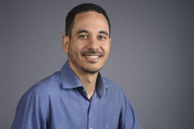 Pessoa vestindo camisa social azul, posicionada em fundo neutro e liso, com enquadramento simples e iluminação uniforme, transmitindo um contexto profissional