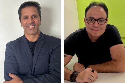 Duas pessoas — uma de blazer escuro e outra com camiseta preta

A primeira veste blazer azul‑escuro e está em frente a um fundo branco.
A segunda está apoiada sobre uma mesa branca, usando camiseta preta e acessórios como pulseiras e anéis. O fundo é verde vivo.
