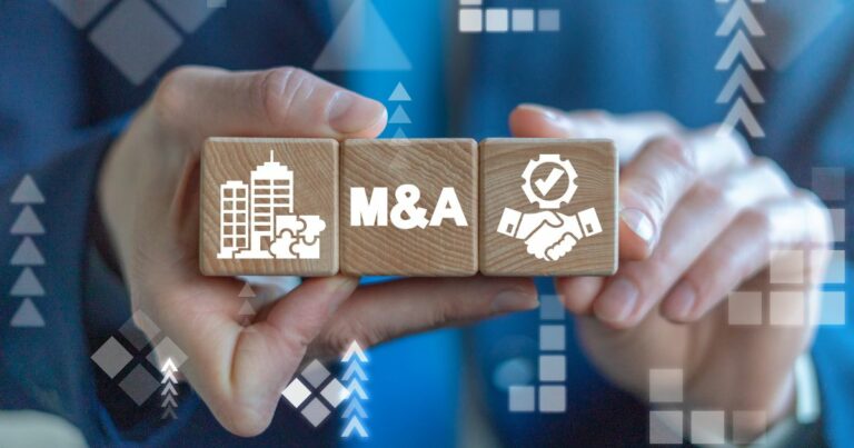 Duas mãos seguram três blocos de madeira alinhados horizontalmente. O bloco central exibe a sigla “M&A”, enquanto os blocos laterais apresentam ícones de edifícios corporativos e um aperto de mãos com símbolo de verificação. Ao fundo, há elementos gráficos abstratos em tons de azul, com setas e formas geométricas, sugerindo crescimento, integração empresarial e processos de fusões e aquisições em um contexto corporativo e financeiro. (M&A)
