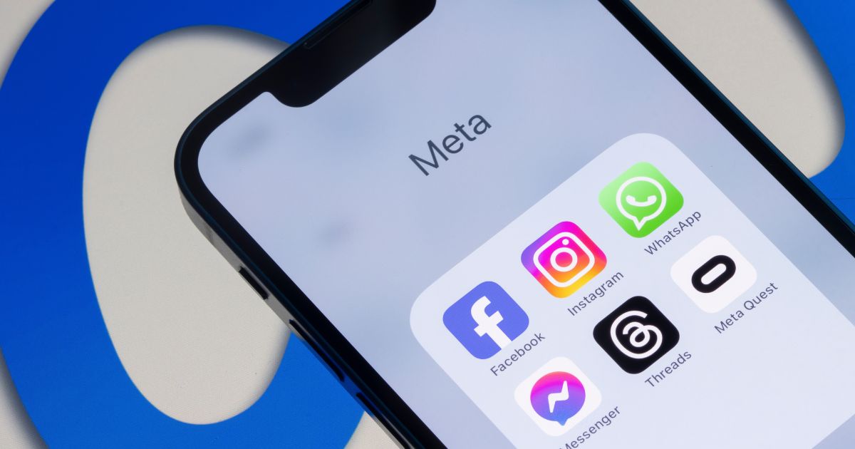 A imagem mostra um smartphone exibindo uma pasta com aplicativos da Meta, sobre um fundo com o logotipo da empresa em azul. Detalhes principais: Tela do dispositivo: Título da pasta: Meta Aplicativos visíveis: Facebook (ícone azul com “f”) Instagram (ícone colorido em degradê) WhatsApp (ícone verde com balão de conversa) Messenger (ícone roxo e azul) Threads (ícone preto com símbolo branco) Meta Quest (ícone branco com símbolo preto) Contexto visual: O fundo apresenta o logotipo da Meta em azul, parcialmente visível, reforçando a identidade da marca. Iluminação e cores: Tons claros e neutros na tela do smartphone contrastando com o azul vibrante do fundo, criando uma composição limpa e moderna. (Meta)