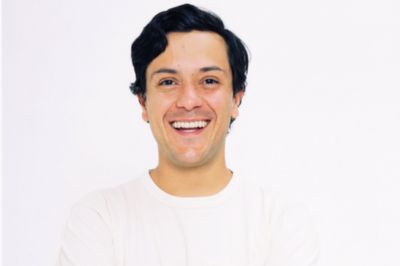 Uma pessoa vestindo camiseta branca está em pé com os braços cruzados diante de um fundo totalmente claro, criando um visual minimalista e limpo.