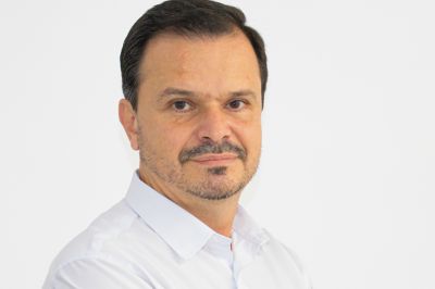 Uma pessoa vestindo camisa social branca aparece em pose profissional contra um fundo claro.