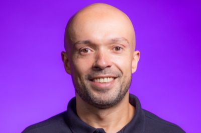 Uma pessoa vestindo camisa polo escura está posicionada contra um fundo roxo vibrante, criando um visual marcante e minimalista.