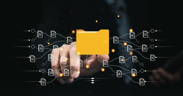 Imagem conceitual em fundo escuro mostrando uma mão humana estendida, tocando uma interface digital flutuante. No centro, há um ícone de pasta amarela destacado, representando um repositório de arquivos ou dados. Ao redor da pasta, aparecem vários ícones de documentos conectados por linhas brancas, formando uma rede de fluxos de informação em ambos os lados. Pequenos pontos de luz em tom alaranjado percorrem as conexões, sugerindo movimentação, integração e organização de dados digitais. A composição remete a conceitos como gestão de documentos, automação de processos e fluxo de informações. (backup)