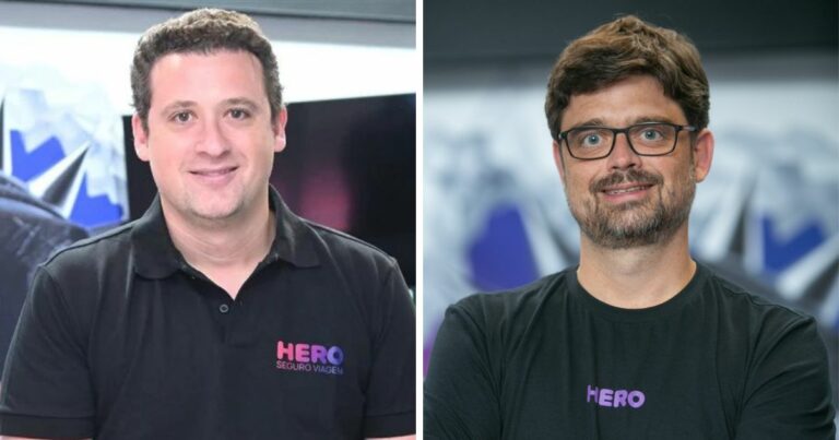 Imagem composta por dois retratos colocados lado a lado. À esquerda, uma pessoa posicionada de frente para a câmera, vestindo camisa polo preta com o logotipo “HERO Seguro Viagem” em cores roxa e rosa. O enquadramento mostra o tronco e o rosto, com expressão neutra e fundo interno desfocado com elementos gráficos. À direita, outra pessoa também de frente para a câmera, vestindo camiseta preta com o logotipo “HERO” em roxo. Essa pessoa usa óculos, tem barba curta e cabelos curtos. O fundo é semelhante ao da primeira imagem, interno e desfocado, sugerindo o mesmo ambiente corporativo. A iluminação é uniforme em ambos os retratos. (Hero Seguros)