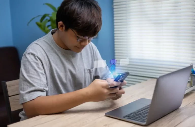 Jovem adolescente usando o celular em um ambiente interno, com laptop e uma pequena figura digital animada ao lado, transmitindo tecnologia e diversão. (ECA Digital)