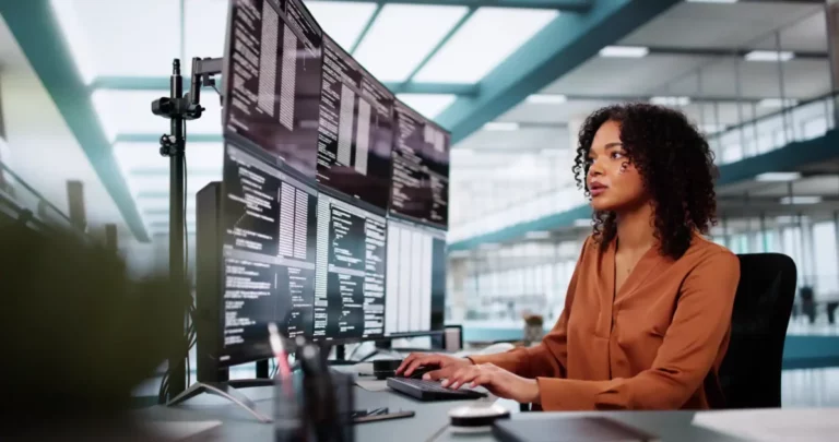 Mulher trabalhando em escritório moderno com múltiplos monitores exibindo códigos de programação, foco e concentração, ambiente de alta tecnologia. curso