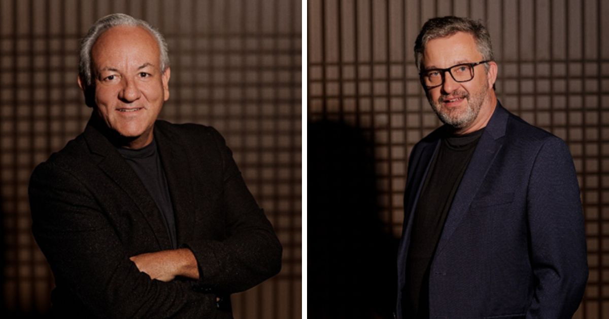 Imagem composta por dois retratos posicionados lado a lado, separados por uma faixa vertical clara. À esquerda, uma pessoa em pé, de frente para a câmera, com cabelos curtos grisalhos, vestindo blazer escuro sobre camiseta escura, com os braços cruzados diante do corpo. À direita, outra pessoa em pé, também de frente para a câmera, com cabelos curtos grisalhos, barba aparada e óculos, vestindo blazer azul escuro sobre camiseta escura. Ambas estão em ambiente interno com fundo padronizado em tons de marrom, formando uma grade geométrica. A iluminação é controlada e direcionada, destacando as pessoas em primeiro plano e criando um retrato de aparência profissional. (agentes)