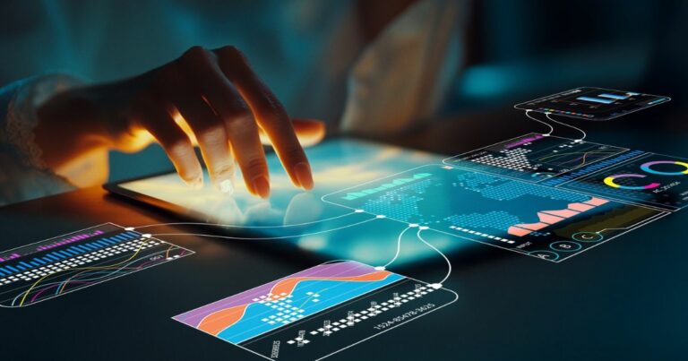 Mão de uma pessoa interagindo com uma tela sensível ao toque sobre uma superfície escura. Sobre a tela, aparecem interfaces digitais translúcidas com gráficos, mapas, linhas de dados e painéis analíticos coloridos conectados entre si, sugerindo visualização e análise de dados. A iluminação cria contraste entre tons quentes na mão e tons frios azuis e verdes nas interfaces, reforçando um contexto tecnológico e digital. (software)