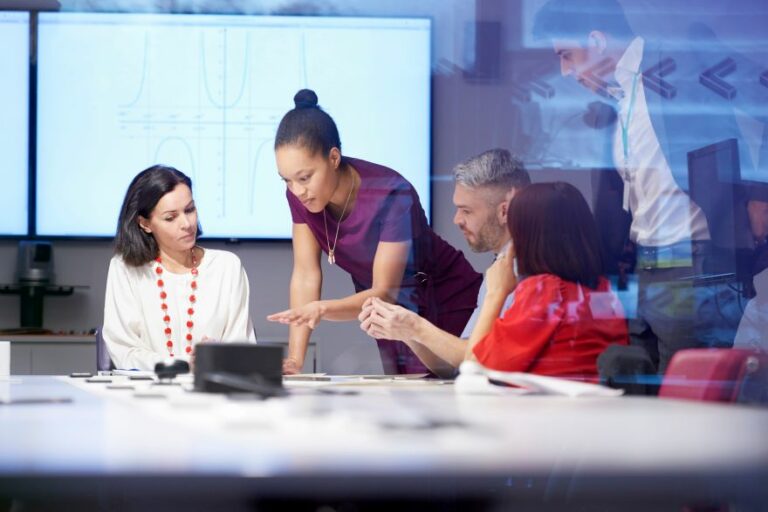 Equipe de profissionais discutindo tecnologia de determinação tributária durante reunião empresarial, com tela de apresentação ao fundo