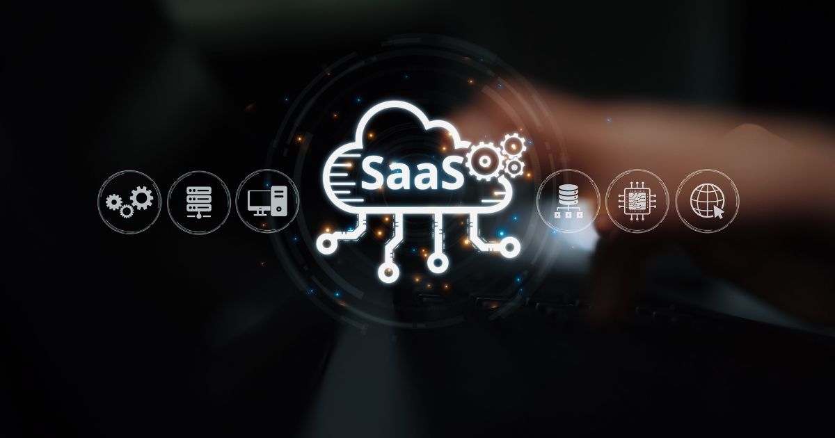 Imagem conceitual em fundo escuro mostrando um ícone luminoso de uma nuvem com a sigla “SaaS” no centro. A nuvem está conectada a pequenos pontos e linhas que se estendem para baixo, representando integração e distribuição de serviços. Ao redor da nuvem, aparecem ícones circulares em tom claro que simbolizam tecnologia e infraestrutura digital, como engrenagens, servidor, banco de dados, chip, globo e rede. Em primeiro plano, desfocado, observa‑se parte de uma mão se aproximando do centro da interface, sugerindo interação humana com uma plataforma de software como serviço. A composição transmite conceitos de computação em nuvem, automação e serviços digitais.
