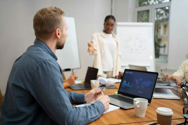 Equipe corporativa em reunião de negócios em escritório moderno, com apresentação estratégica e análise de dados em notebook. Ambiente colaborativo de trabalho, treinamento empresarial e tomada de decisão em equipe.