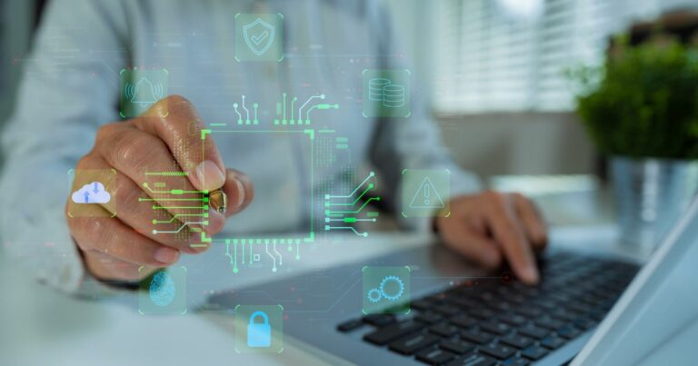 Mão de uma pessoa segurando uma caneta e interagindo com uma interface digital projetada no ar, enquanto outra mão utiliza um computador portátil ao fundo. No centro, há um quadrado com linhas e circuitos luminosos em verde, lembrando um chip eletrônico. Ao redor, aparecem ícones translúcidos como nuvem, impressão digital, cadeado, engrenagens, banco de dados e alertas, conectados por linhas digitais. O ambiente é interno, com iluminação suave e fundo desfocado, sugerindo tecnologia, segurança da informação e processamento de dados. (ameaças)