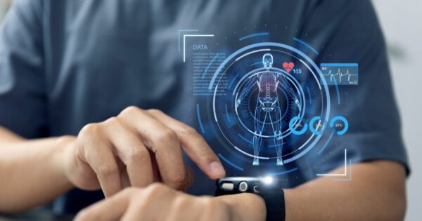 Pessoa utilizando um smartwatch no pulso, tocando a tela com o dedo indicador da outra mão. Sobreposta à imagem, há uma interface digital em tons de azul com a representação de um corpo humano em estilo wireframe, destacando o esqueleto. Ao redor, aparecem gráficos circulares, barras de progresso, ícones e um monitoramento de frequência cardíaca com números como ‘115’. O fundo é desfocado, com foco no braço, no relógio e nos elementos visuais, sugerindo tecnologia wearable e acompanhamento de dados de saúde.