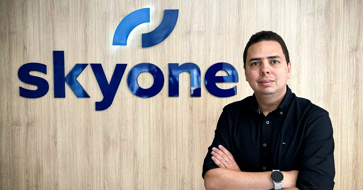 Profissional posando com braços cruzados em frente ao logotipo da Skyone em escritório moderno, destacando identidade corporativa e ambiente empresarial.