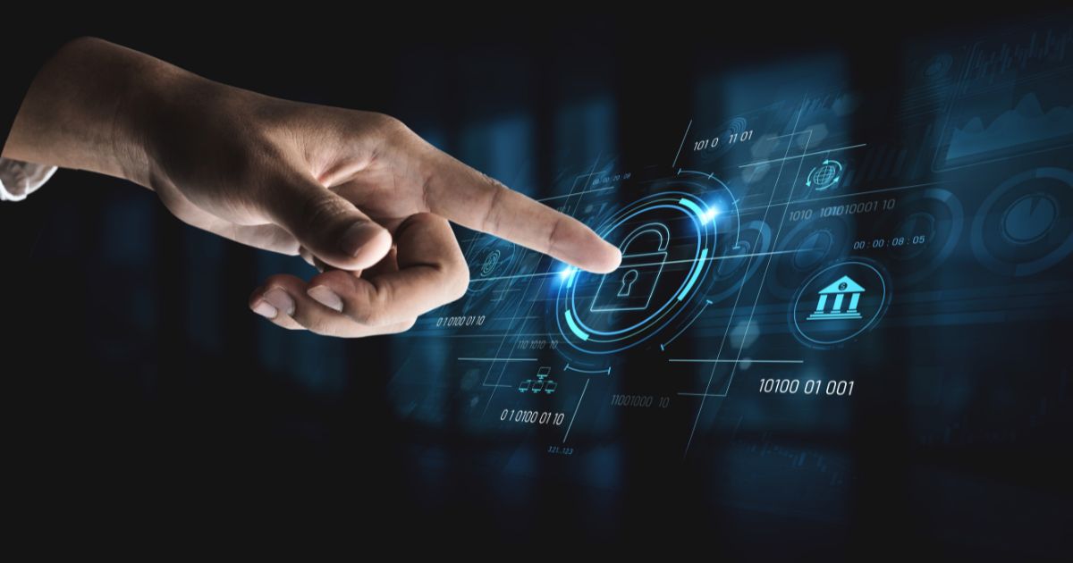 Imagem em close de uma mão estendida na horizontal, com o dedo indicador apontando para a direita e tocando uma interface digital holográfica. No centro da interface, há um ícone de cadeado envolvido por círculos e elementos gráficos luminosos em tons de azul, sugerindo proteção e segurança. Ao redor do cadeado, aparecem símbolos e elementos visuais adicionais, como códigos binários (“0” e “1”), gráficos e um ícone estilizado de um edifício institucional, possivelmente representando sistemas financeiros ou governamentais. As informações estão distribuídas em camadas translúcidas, criando um efeito de profundidade tecnológica. O fundo é escuro e desfocado, com tons predominantes de azul e preto. A iluminação destaca a mão e os elementos digitais, reforçando o conceito de segurança cibernética, proteção de dados e interação com sistemas tecnológicos avançados. (parceiro)