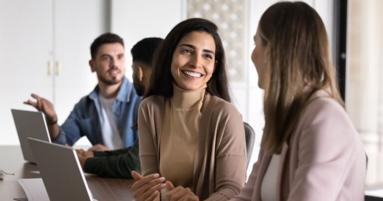 Profissionais reunidos em ambiente corporativo colaborativo, participando de reunião com notebooks sobre a mesa, destacando trabalho em equipe, comunicação interna, desenvolvimento de talentos e cultura organizacional.