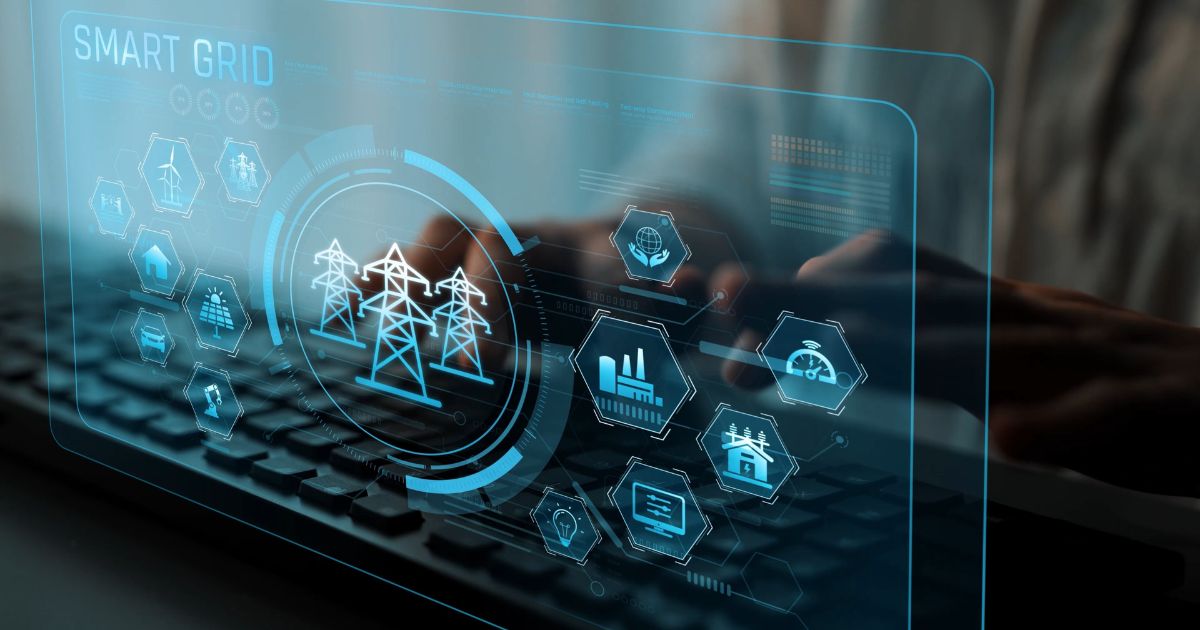 Mais de 60% dos fornecedores de energia utiliza IA para prever ganhos em eficiência e operação, aponta estudo 4 Imagem conceitual sobre redes elétricas inteligentes (smart grids). Em primeiro plano, um teclado de computador aparece desfocado, enquanto uma interface digital semitransparente em tons de azul é sobreposta à cena. No centro da interface há um ícone representando torres de transmissão de energia elétrica. Ao redor, diversos ícones hexagonais ilustram elementos conectados à rede, como turbinas eólicas, painéis solares, residências, veículos elétricos, fábricas, medidores inteligentes e símbolos de sustentabilidade. No canto superior esquerdo, aparece o texto “SMART GRID”. Ao fundo, é possível ver mãos interagindo com um dispositivo, parcialmente desfocadas. A composição destaca a integração entre tecnologia digital, monitoramento em tempo real e infraestrutura energética inteligente.