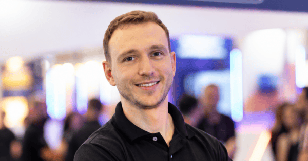 Eduardo Diederichsen, novo general manager da Syonet, empresa do Grupo Webmotors, aparece sorrindo e de braços cruzados durante um evento do setor automotivo, vestindo camisa polo preta com o logotipo da Syonet. Ao fundo, estão o estande da companhia, a identidade visual da marca e participantes do evento desfocados. O executivo assume a liderança da operação após atuar como CTO, com foco na evolução tecnológica e na integração da Syonet ao Grupo Webmotors. (Eduardo Diederichsen, Syonet, Webmotors, Liderança, Tecnologia, Transformação Digital, Mercado Automotivo)